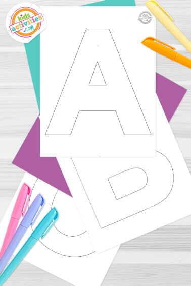 Black and white printed cardboard letter templates on top of blue-green and purple sheets with assorted markers on a dark grey background. printed pdf version from Kids activities blog.