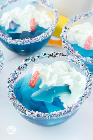Blue Jello Dessert with gummy sharks in a clear glass dessert bowl with sprinkles around the rim