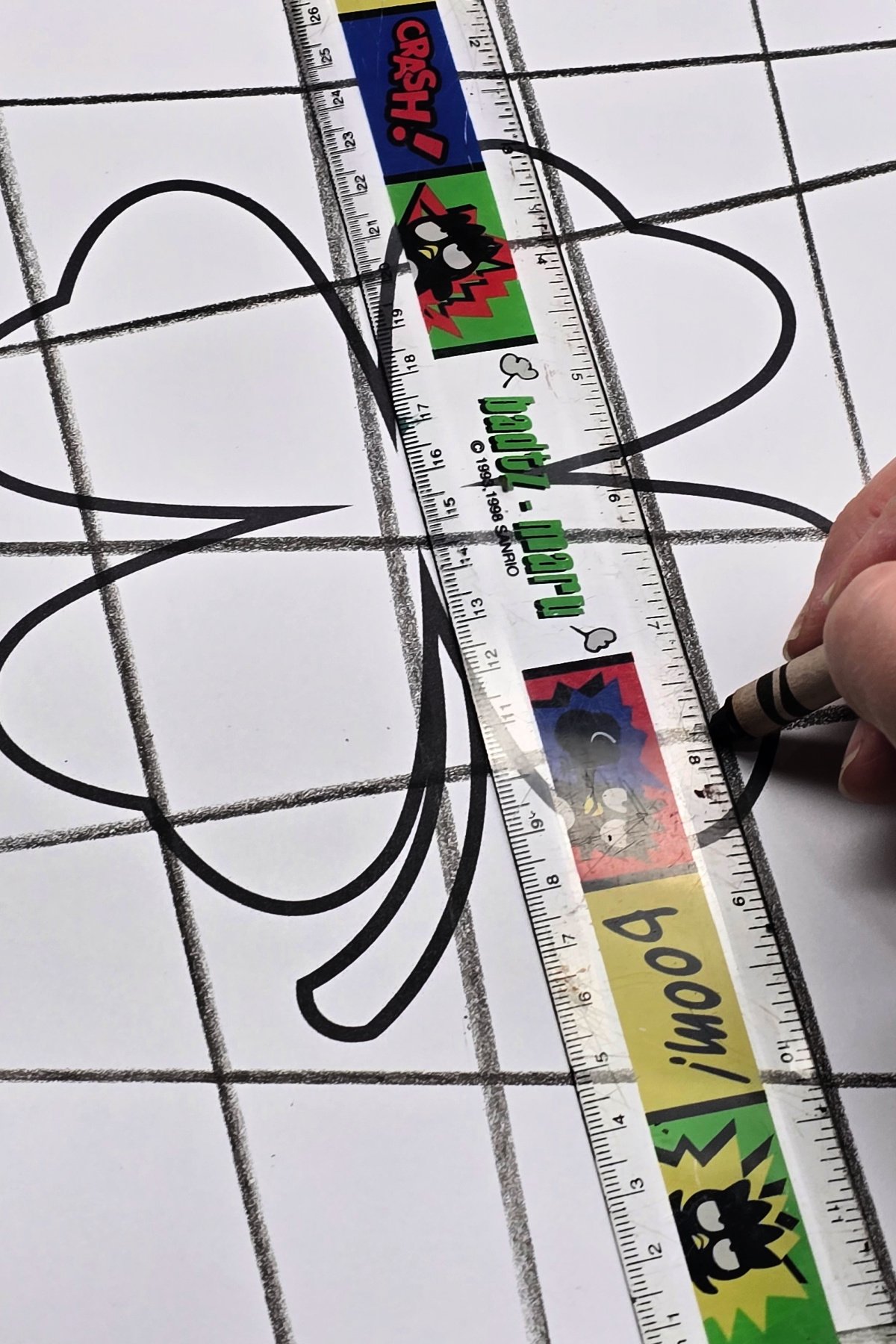 using a black crayon and ruler to draw vertical and horizontal lines to create a grid over the shamrock design - kids activities blog