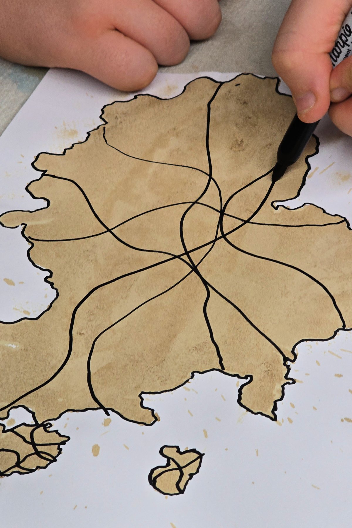 step 4 - boy using a permanent marker to draw wavy lines through a dry coffee spill on cardstock - kids activities blog
