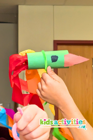 Flying Rocket Art Project. Image of kids hand holding green rocket art flying in air. - kidsactivities.com